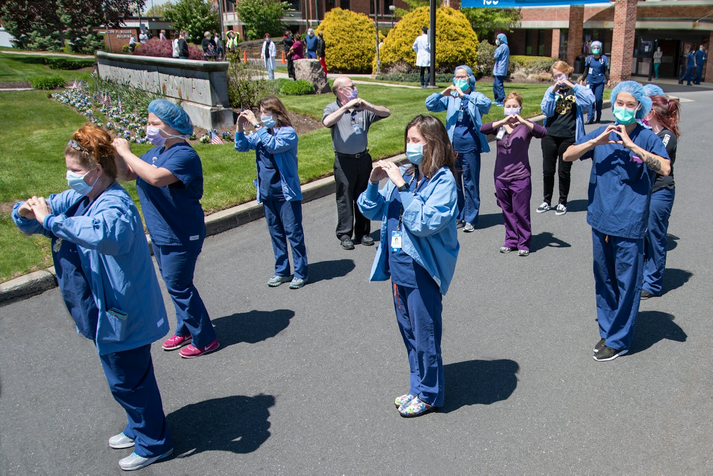 Diverse healthcare workers form heart shapes with hands outdoors.